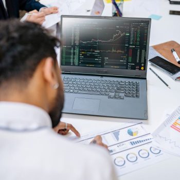 Business professionals analyzing stock charts and graphs on a laptop in an office setting.